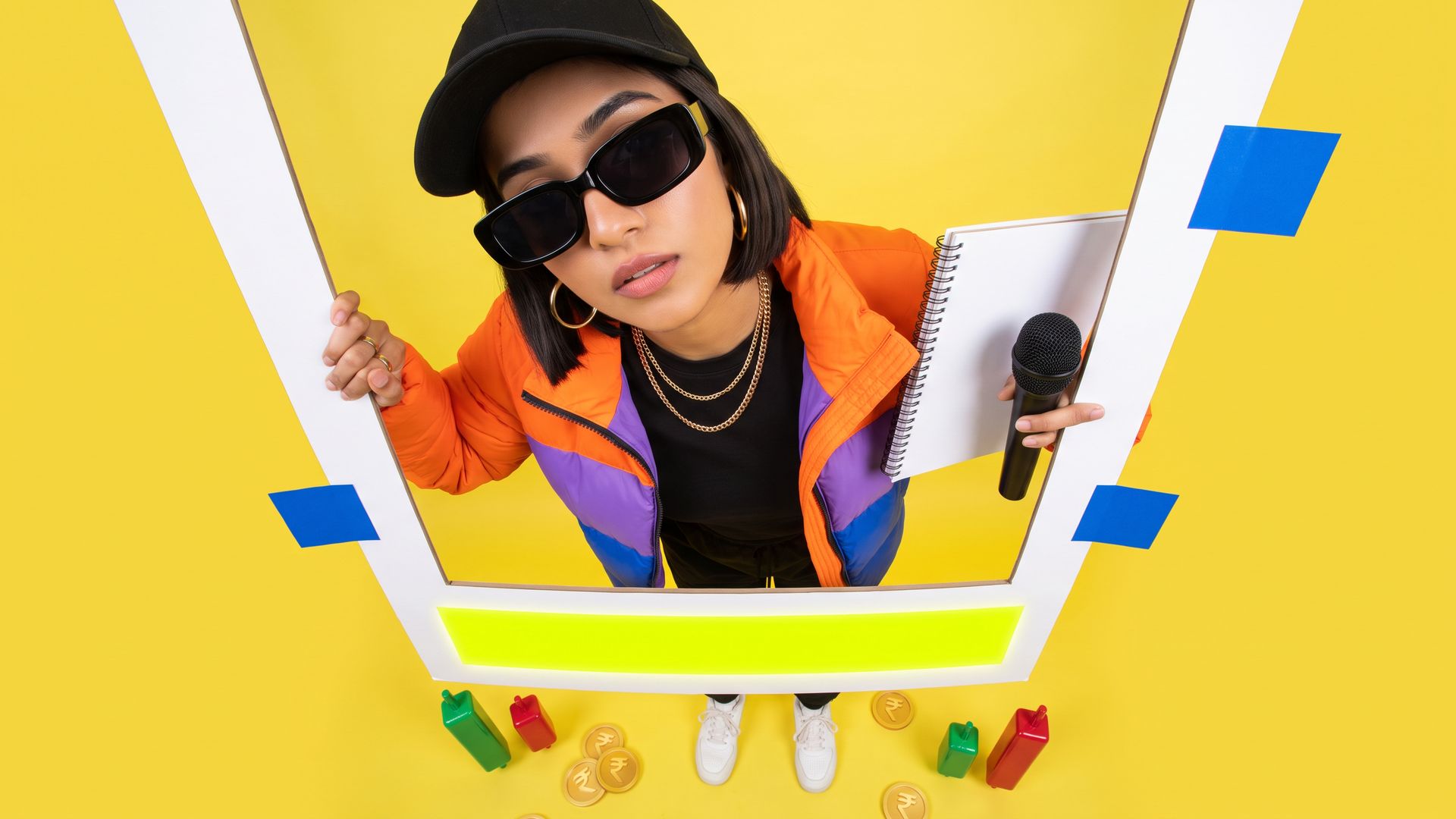 A young Indian marketer leans into a fisheye lens holding a blank social-post frame with a highlighted disclaimer strip, a sales deck and mic under her arm.